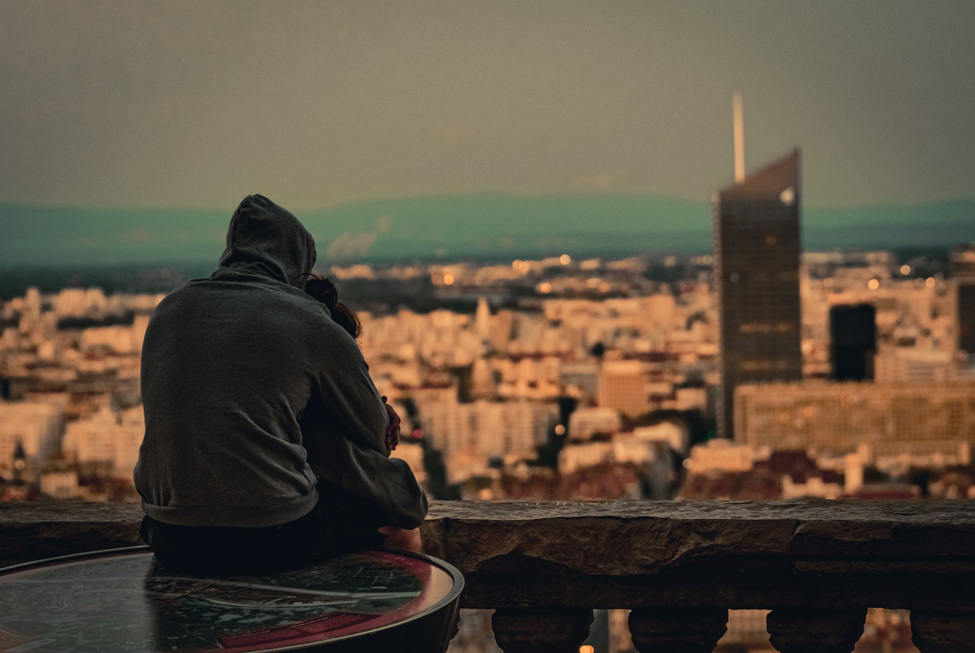 person in gray hooded jacket facing buildings at daytime